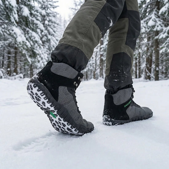 Hombre caminando en la nieve con botas barefoot Saguaro Vitality V gris, demostrando resistencia y agarre en climas extremos.