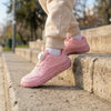 Niña jugando al aire libre con zapatillas respetuosas Saguaro Forestep I rosa, calzado resistente para senderismo y plaza.