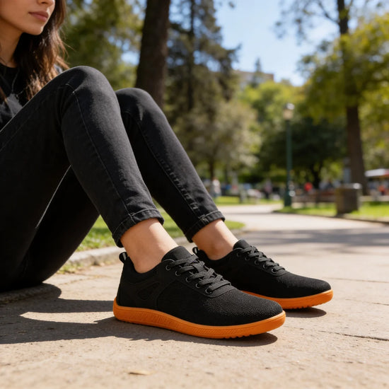 Primer plano de una mujer sentada en un parque con zapatillas barefoot negras.
