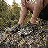Hombre descansando en exteriores usando zapatos minimalistas verdes Saguaro Active II.