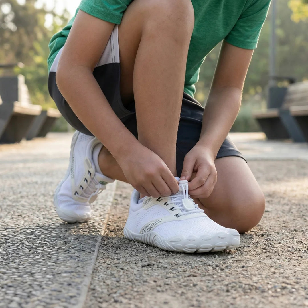 Niño abrochándose sus zapatillas barefoot Saguaro Kids Free blancas, destacando la autonomía infantil y el ajuste fácil con velcro.