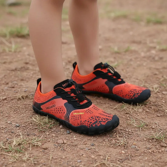 Niño utilizando Zapatillas barefoot Saguaro Kids Fast I naranjas en tierra