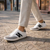 Mujer usando zapatillas barefoot ZZfaber Niza I blanco con negro en exterior.
